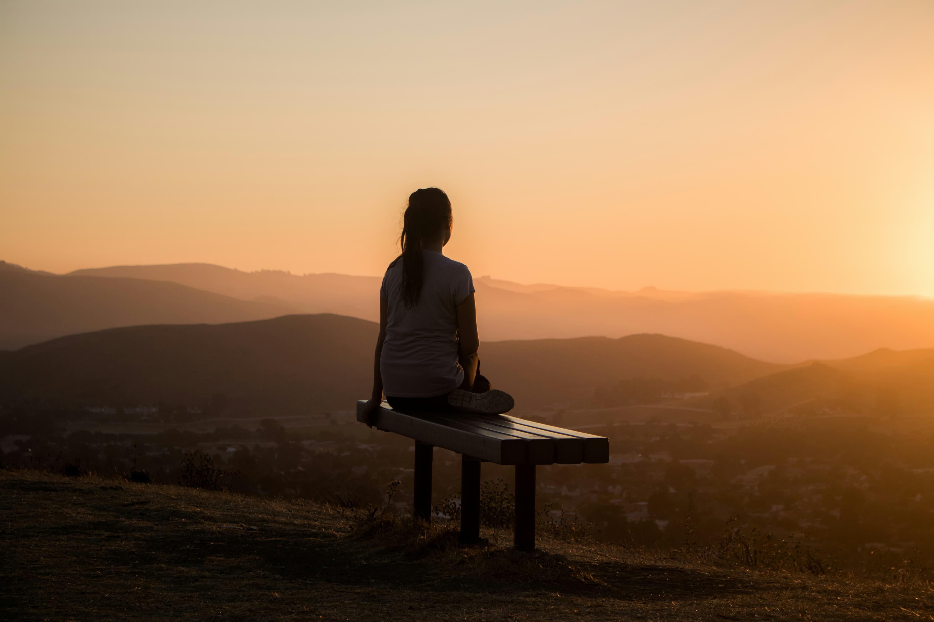 Background image of a woman sitting on a bench watching the sunset.
